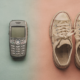 A retro smartphone and vintage sneakers arranged on a split colored surface blending two eras