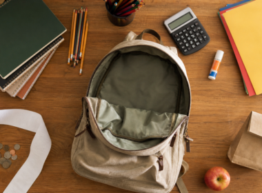Back to school spending shown as an empty canvas backpack, school supplies and a long blank receipt on a kitchen table