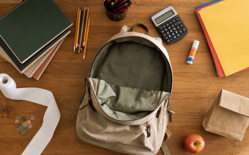 Back to school spending shown as an empty canvas backpack, school supplies and a long blank receipt on a kitchen table