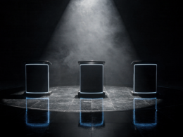 Three illuminated competition podiums in a hazy dark television studio with the center one spotlit, illustrating the BB Blockbuster on Big Brother 28