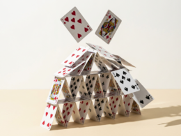 Close macro photograph of a house of cards collapsing on a pale cream surface
