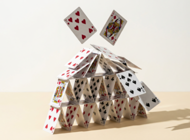 Close macro photograph of a house of cards collapsing on a pale cream surface