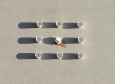 Overhead grid of ten white ceramic cups with one tipped over, long hard morning shadows