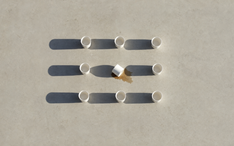 Overhead grid of ten white ceramic cups with one tipped over, long hard morning shadows
