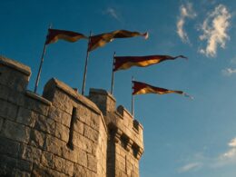 Low angle view of a medieval castle turret with crimson and gold pennants against a bright sky