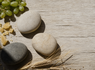 Big Brother 28 recap image of three river stones, grapes and beeswax on sunlit oak planks