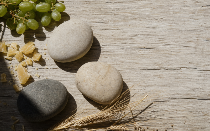 Big Brother 28 recap image of three river stones, grapes and beeswax on sunlit oak planks