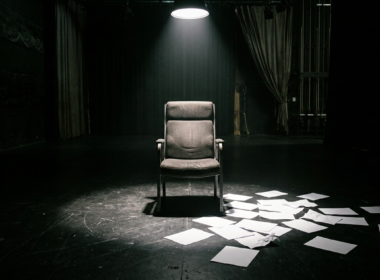 Big Brother 28 eviction illustrated by an empty reality television interview chair under a hard spotlight with paper ballots scattered on a dark studio floor