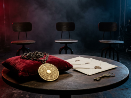 Big Brother 28 spoilers concept with a gold veto medallion on a red velvet cushion, three sealed envelopes and three empty chairs on a dark studio set