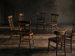 Big Brother 28 Mosh Pit alliance falling apart shown by a circle of seven wooden chairs with two turned away, breaking the ring