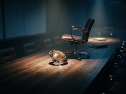 Big Brother 28 spoilers image showing a faceted diamond on a dark boardroom table with one empty chair pushed back