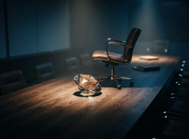 Big Brother 28 spoilers image showing a faceted diamond on a dark boardroom table with one empty chair pushed back