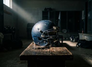 A football helmet resting on a bench in a dim locker room with a single shaft of light