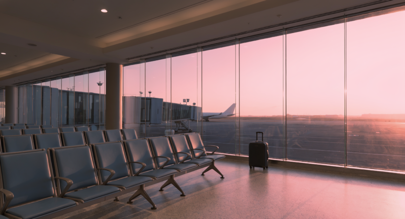 Cheapest week to fly shown as a nearly empty airport departure gate at dawn with a single rolling suitcase