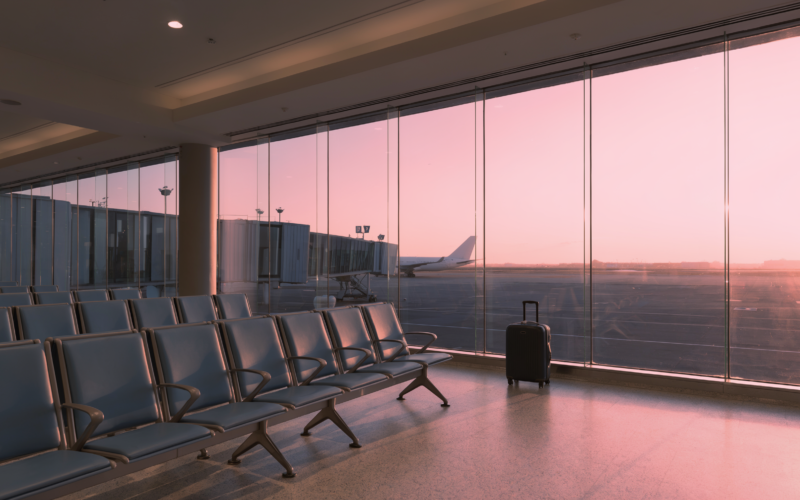 Cheapest week to fly shown as a nearly empty airport departure gate at dawn with a single rolling suitcase