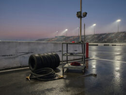 Connor Zilisch Hendrick signing shown by an empty pit box at dusk with tires and a coiled fuel hose