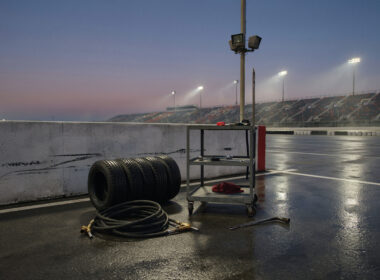 Connor Zilisch Hendrick signing shown by an empty pit box at dusk with tires and a coiled fuel hose
