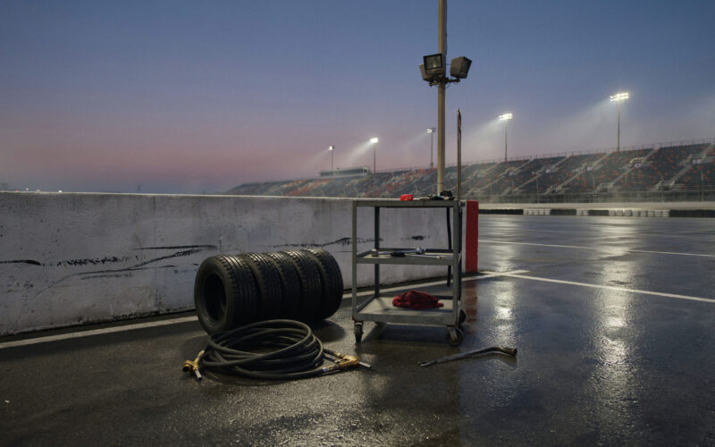 Connor Zilisch Hendrick signing shown by an empty pit box at dusk with tires and a coiled fuel hose