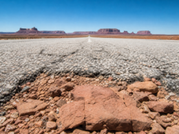 Worm eye view down an empty desert highway toward red rock mesas under a brilliant blue sky