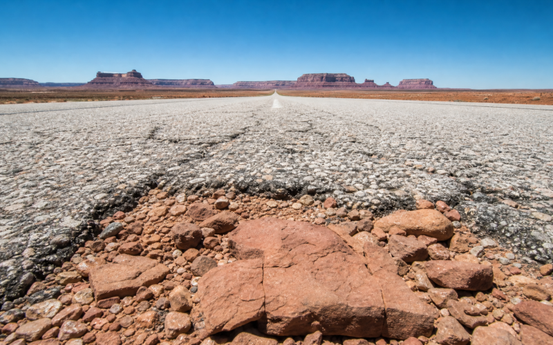 Worm eye view down an empty desert highway toward red rock mesas under a brilliant blue sky