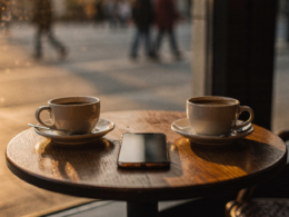 Two coffee cups at a cafe window with a phone face down as people step away from dating apps