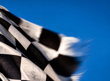 Macro of a black and white checkered flag rippling in motion blur against a bright blue sky