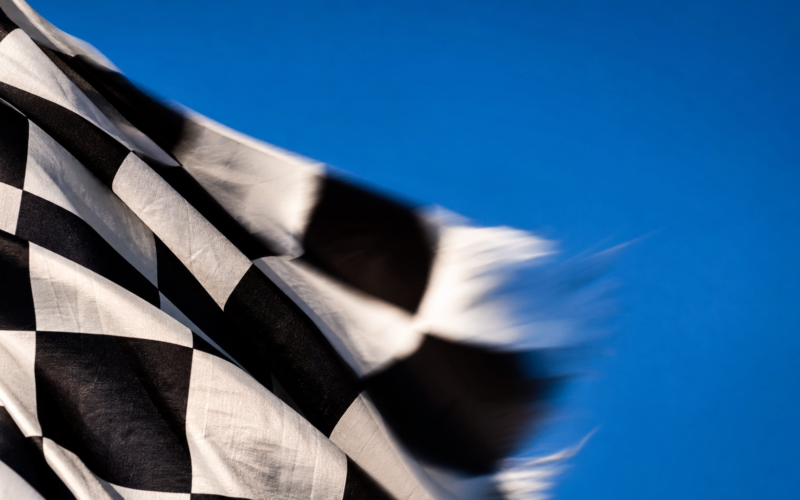 Macro of a black and white checkered flag rippling in motion blur against a bright blue sky