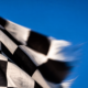 Macro of a black and white checkered flag rippling in motion blur against a bright blue sky