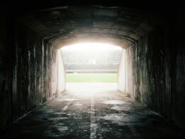 View from inside a dark concrete stadium tunnel looking out toward a blown out bright field