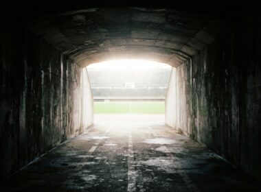 View from inside a dark concrete stadium tunnel looking out toward a blown out bright field