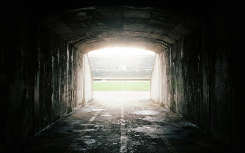 View from inside a dark concrete stadium tunnel looking out toward a blown out bright field
