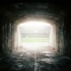 View from inside a dark concrete stadium tunnel looking out toward a blown out bright field