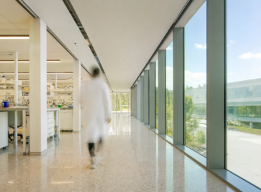 Bright sunlit research laboratory corridor with a motion blurred figure in a white coat walking away