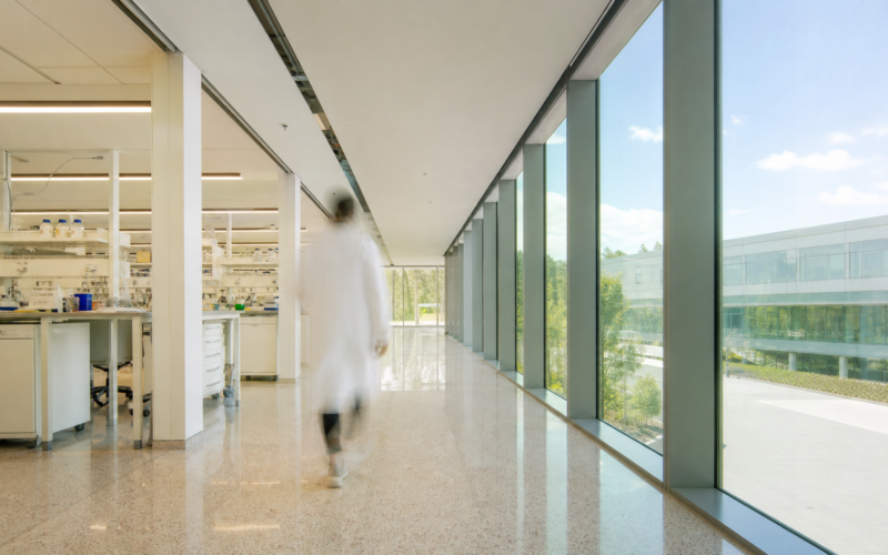 Bright sunlit research laboratory corridor with a motion blurred figure in a white coat walking away