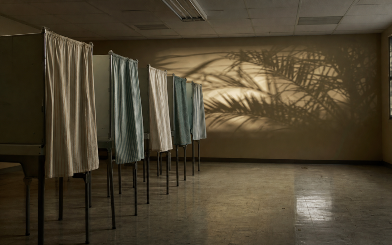 Florida primary governor race shown by empty voting booths in a polling place at night with palm shadows on the wall