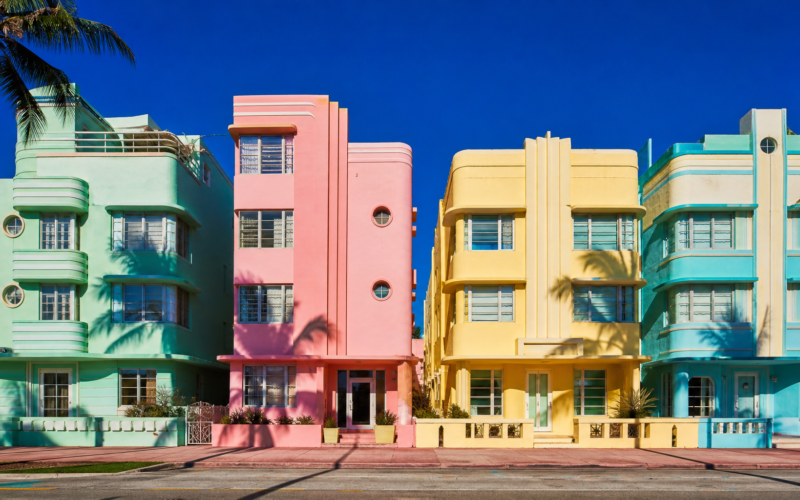 Row of pastel art deco facades in mint green flamingo pink and butter yellow under blazing midday sun