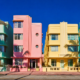 Row of pastel art deco facades in mint green flamingo pink and butter yellow under blazing midday sun
