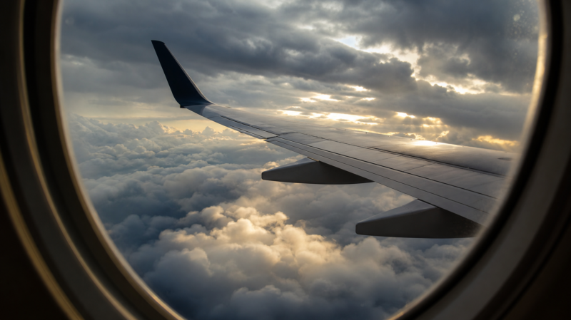 Turbulence nowcast illustrated by an airliner wing seen through a cabin window above a churning layer of storm cloud tops