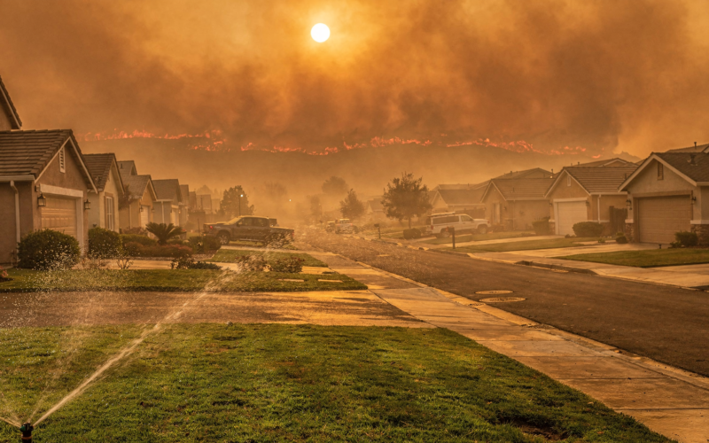 Hawk Fire Reno concept, suburban street under an orange smoke sky with a sprinkler running