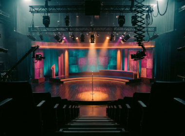 Empty late night television studio seen from the back of the audience risers under teal and magenta stage light