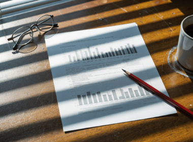 July jobs report bar chart printed on a desk with a red pencil, reading glasses and a cold cup of coffee