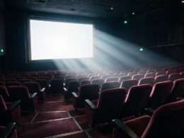 A dark cinema hall with a glowing blank screen and dramatic beams of light