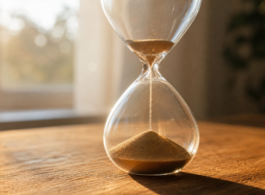 Backlit hourglass on an oak table with sand falling through the neck