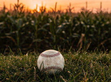 Field of Dreams Game concept: a baseball on grass beside a cornfield at golden dusk