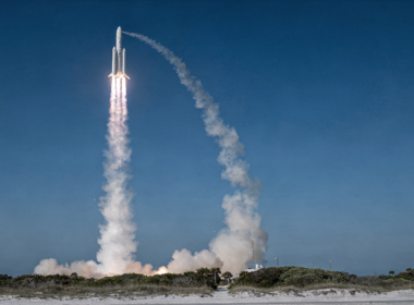 Heavy lift rocket climbing through a clear blue morning sky trailing a white exhaust column