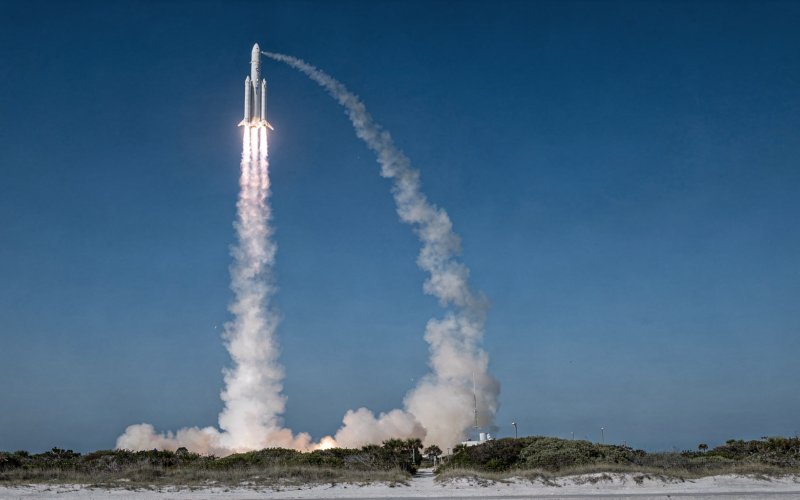 Heavy lift rocket climbing through a clear blue morning sky trailing a white exhaust column