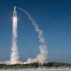 Heavy lift rocket climbing through a clear blue morning sky trailing a white exhaust column