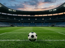 A soccer ball resting on a pristine green pitch inside a large empty stadium at dusk