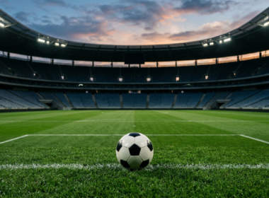 A soccer ball resting on a pristine green pitch inside a large empty stadium at dusk