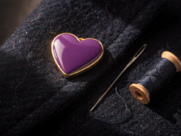 Purple Heart Day medal with gold trim resting on a folded navy wool coat beside a sewing needle and thread